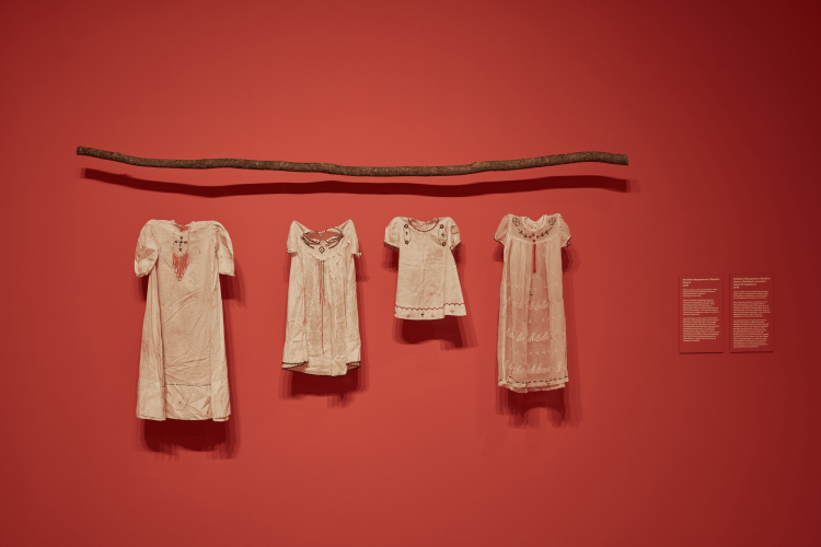 Jobena Petonoquot, Resilient Repugnance: Baptism Gowns, 2018, fabric, beads, earth, birch branch, cedar (comprised of four baptismal dresses suspended from a branch). Branch: 195.58 cm. Dresses: 59.7 x 25.4 cm each. Courtesy of the Artist. Photo: Rémi Thériault.